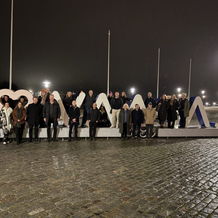 A group of people pose together outdoors at night in front of large decorative letters on a cobblestone street, illuminated by streetlights.