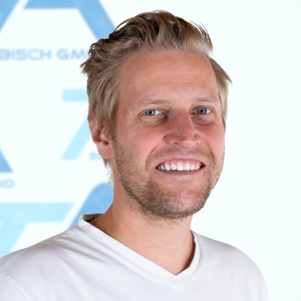 Ein lächelnder Mann mit blonden Haaren und einem hellen Bart, der ein weißes Hemd trägt, steht vor einem verschwommenen weiß-blauen Hintergrund mit Textfragmenten und Formen.
