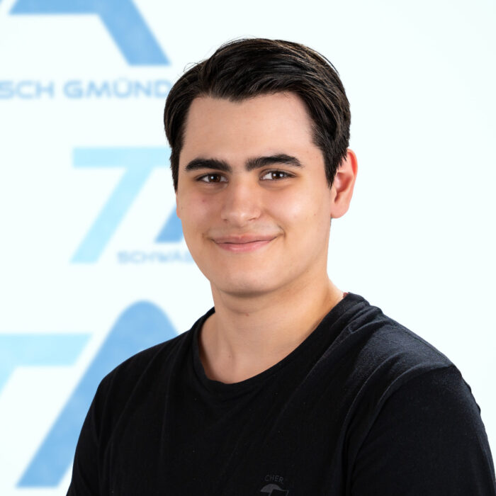 Ein junger Mann in einem schwarzen T-Shirt lächelt in die Kamera.