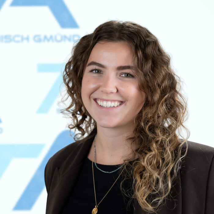 Eine lächelnde Frau mit schulterlangen Locken, die einen dunklen Blazer über einem schwarzen Oberteil trägt.
